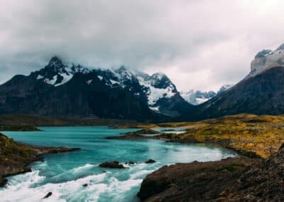 Turquoise river flowing through Patagonia landscape with dramatic cloudy mountains